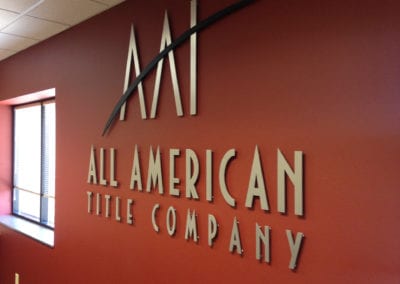 ADA interior sign on a orange wall. The sign is individual gold letters for All American Title Company