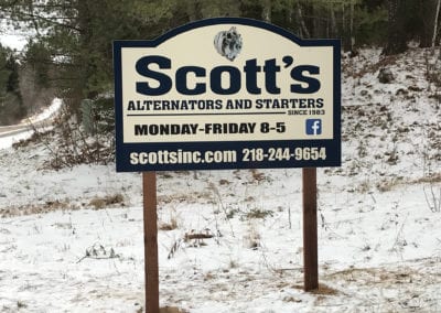 vinyl sign on in the grass on wooden stand. Sign is cream and blue and advertising Scott's Alternators and Starters